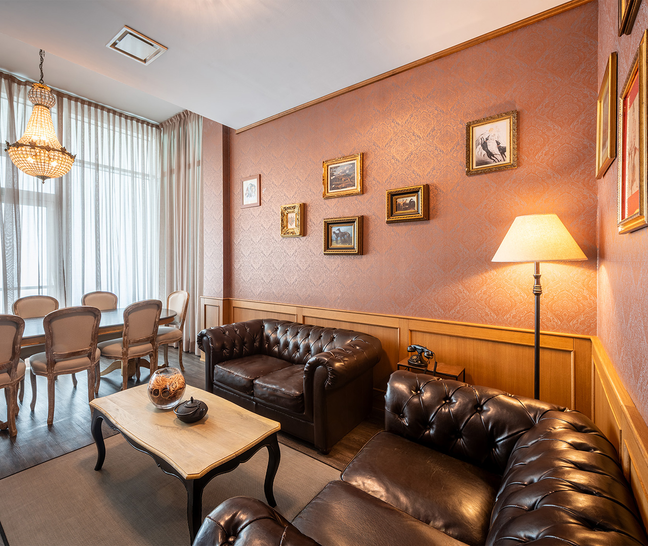 sigar room elegante con divani in pelle scura, tavolo basso, lampada da terra e parete decorata con quadri dorati.