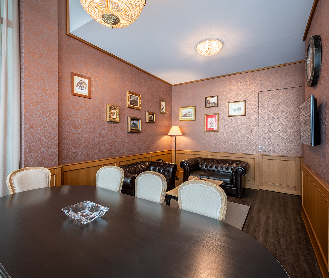 sigar room raffinata con tavolo scuro, sedie imbottite, divani in pelle e pareti rivestite con quadri.