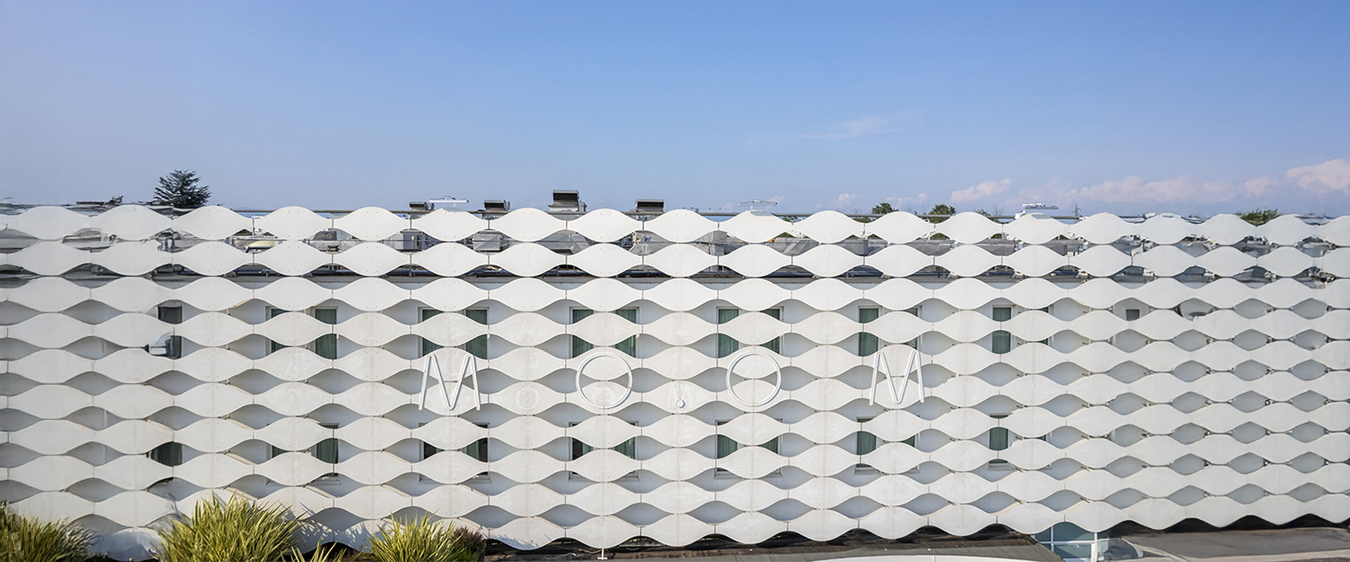 The exterior of the MOOM Hotel, showcasing its iconic white wave-patterned facade under a blue sky