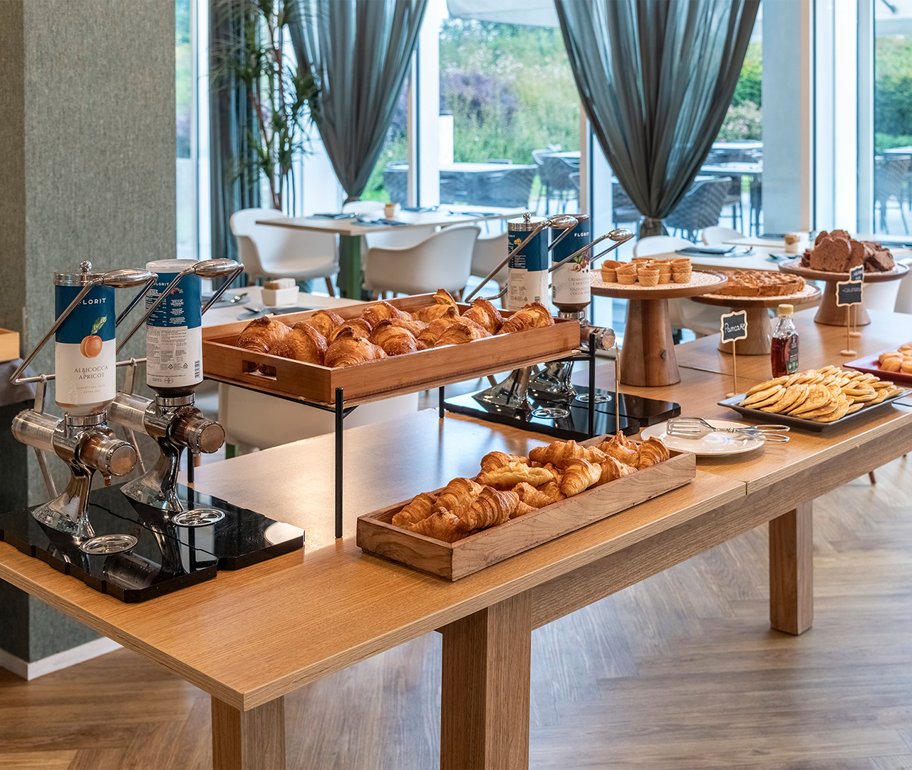 Ricco buffet per la colazione allestito nella luminosa sala ristorante, con vista sul giardino