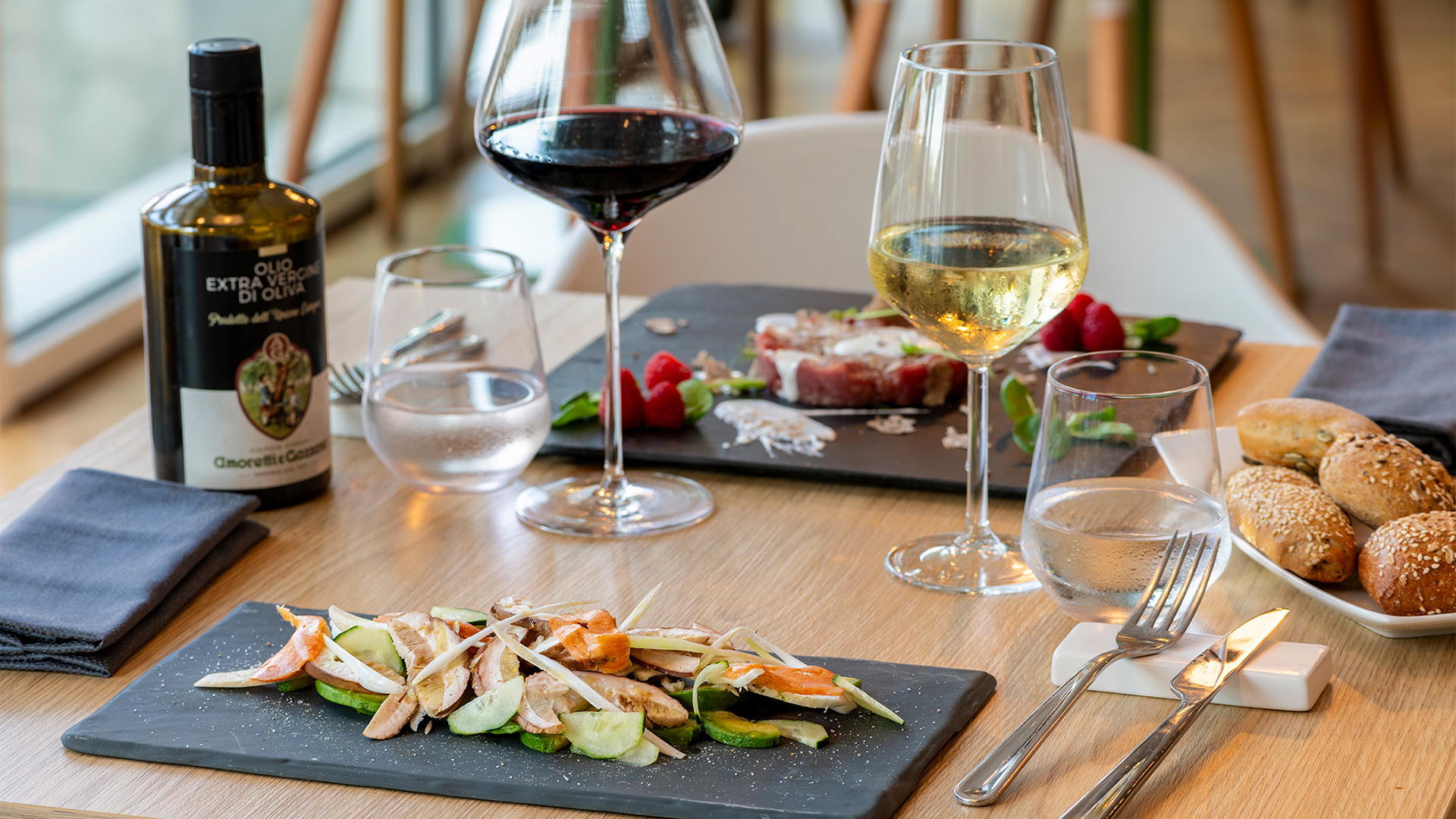 Tavola apparecchiata con piatti gourmet, pane fresco e calici di vino rosso e bianco