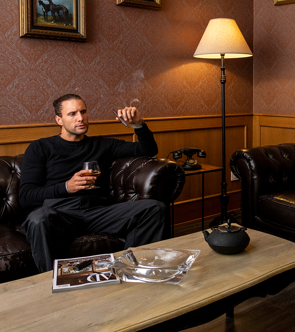 Ospite si rilassa nella cigar room, seduto su un divano in pelle con sigaro e distillato