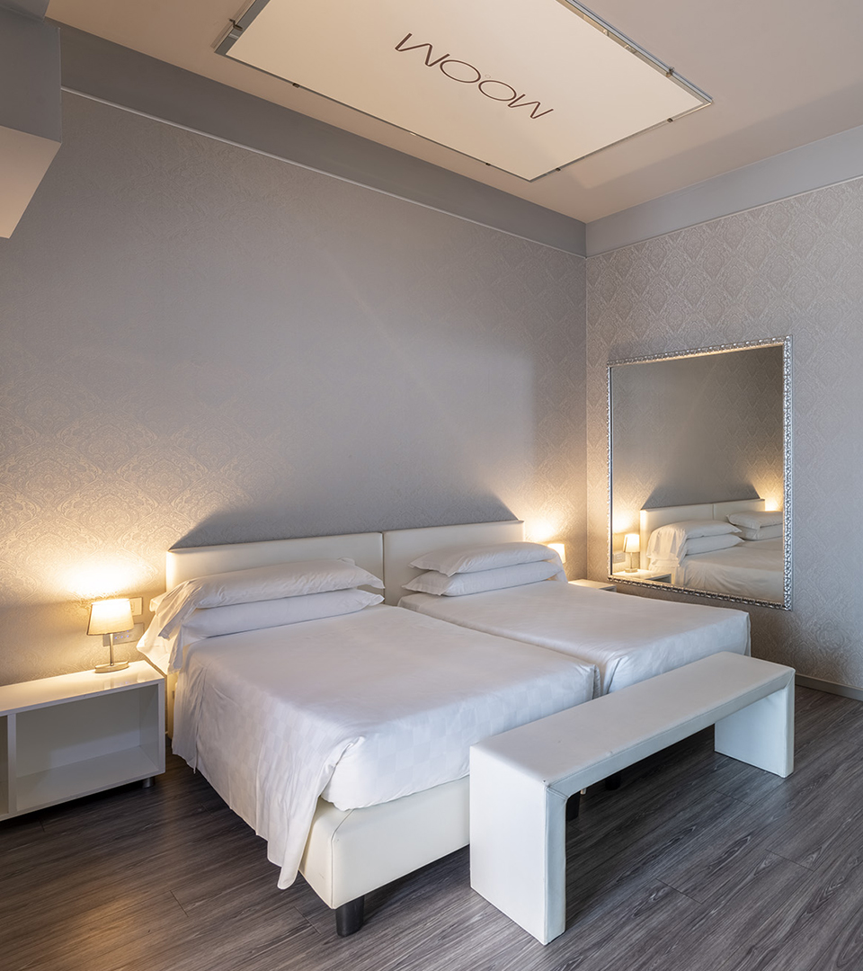 Camera Deluxe con letti singoli affiancati, panca ai piedi del letto, grande specchio a parete e illuminazione soffusa con abat-jour laterali