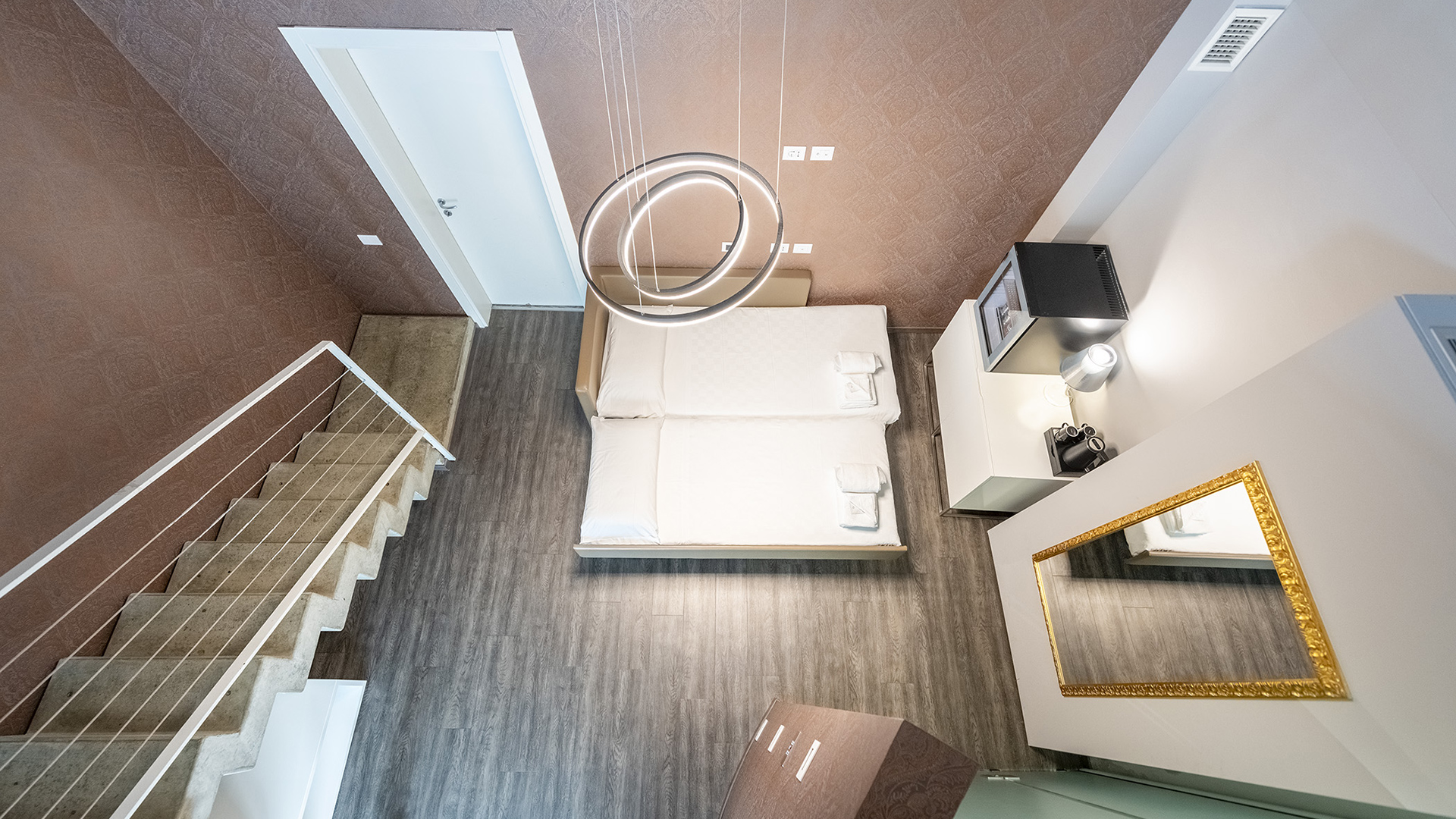 Elegante camera del MO.OM Hotel con due letti, pareti marroni, pavimento in legno e dettagli dorati