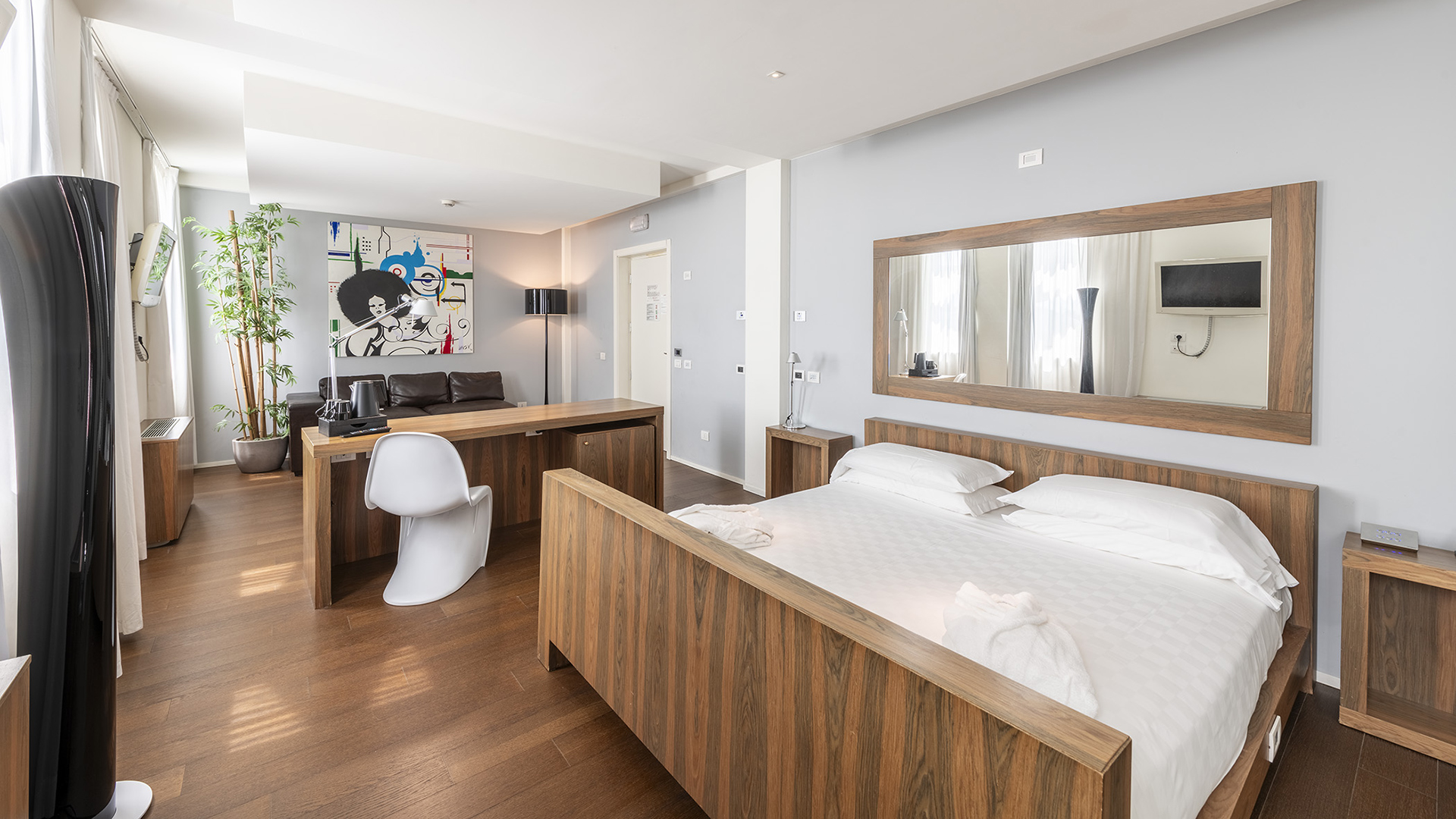 Suite Superior con letto matrimoniale in legno, scrivania centrale con sedia di design, zona living con divano in pelle, grande specchio a parete e ampie finestre luminose
