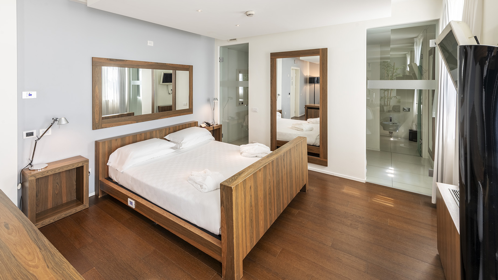 Suite Superior con letto matrimoniale in legno, comodini coordinati, grande specchio a parete, pavimento in parquet e bagno con pareti in vetro a vista