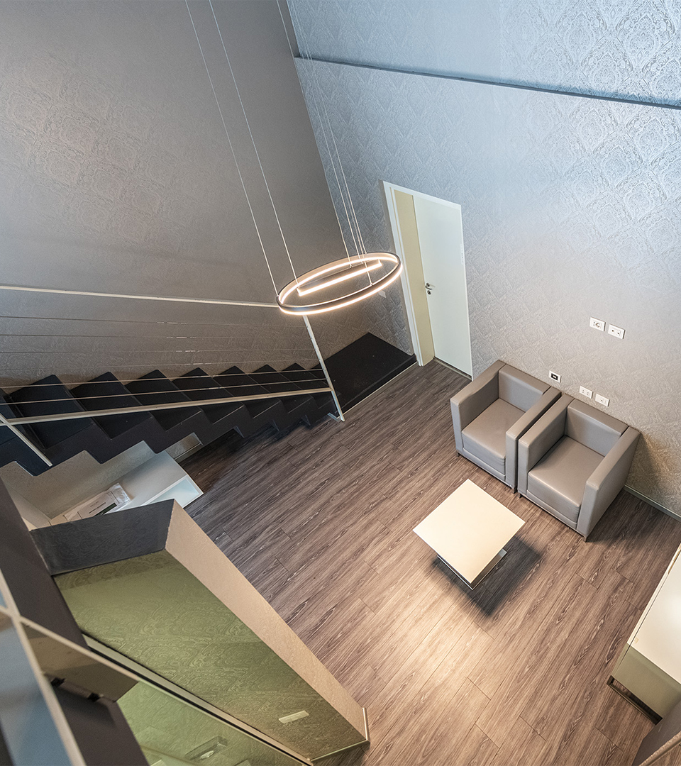 Duplex suite featuring a lower-level living area, internal staircase, armchairs with a central coffee table, and a circular designer pendant lamp.