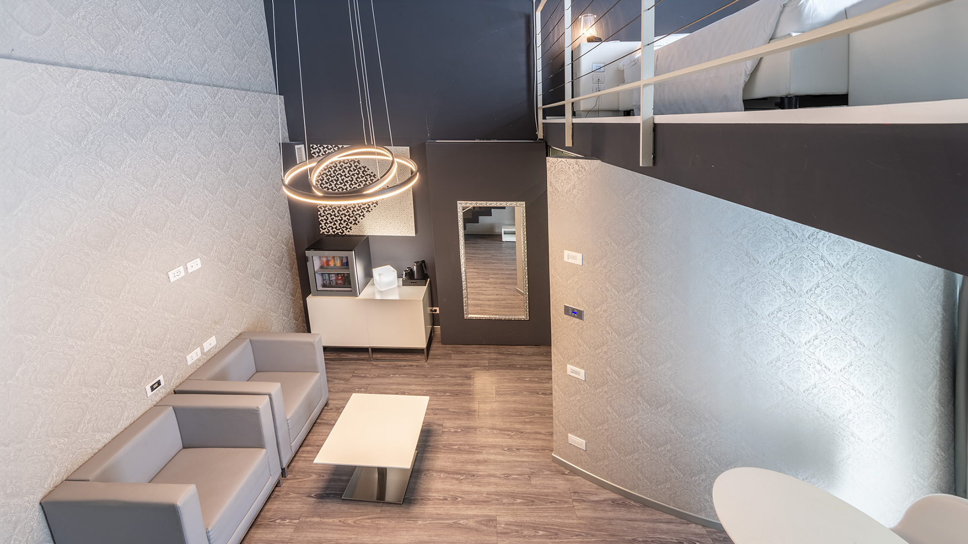 Luxurious living room of a two-level suite: gray walls, circular lamps, wooden floor, two gray sofas, and a white coffee table